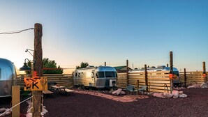 A campsite with RVs and trailers, a wooden fence, and a gravel ground. - Airstream w/ Private Hot Tub (Unit K) - 4 Person Airstream with Private Hot Tub (Williams)
