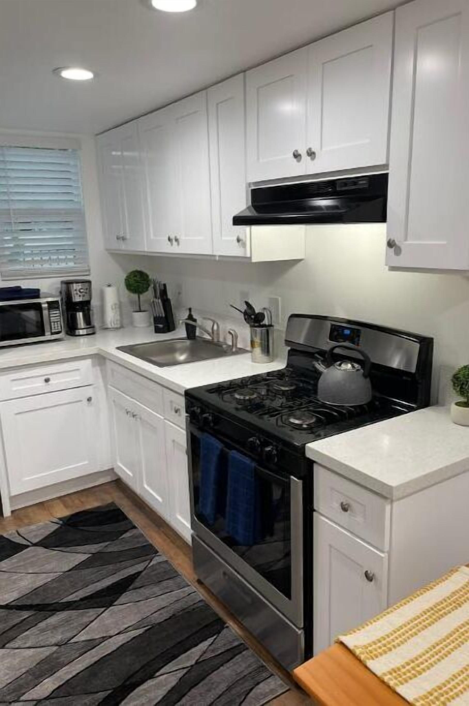 A modern kitchen with white cabinets, a stainless steel stove, and a microwave.