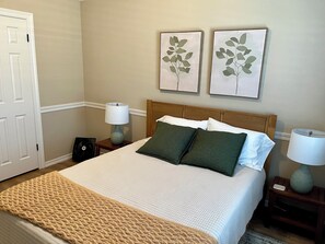Una cama bien tendida con una decoración en blanco y verde, dos lámparas fijadas a la pared y una puerta a la izquierda.