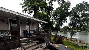 A lakeside cabin with a deck, outdoor seating, and a grill area. - Waterfront 2BR Cottage: Fire Pit, Grill & Dock -Boat Slip Available additional (Monticello)