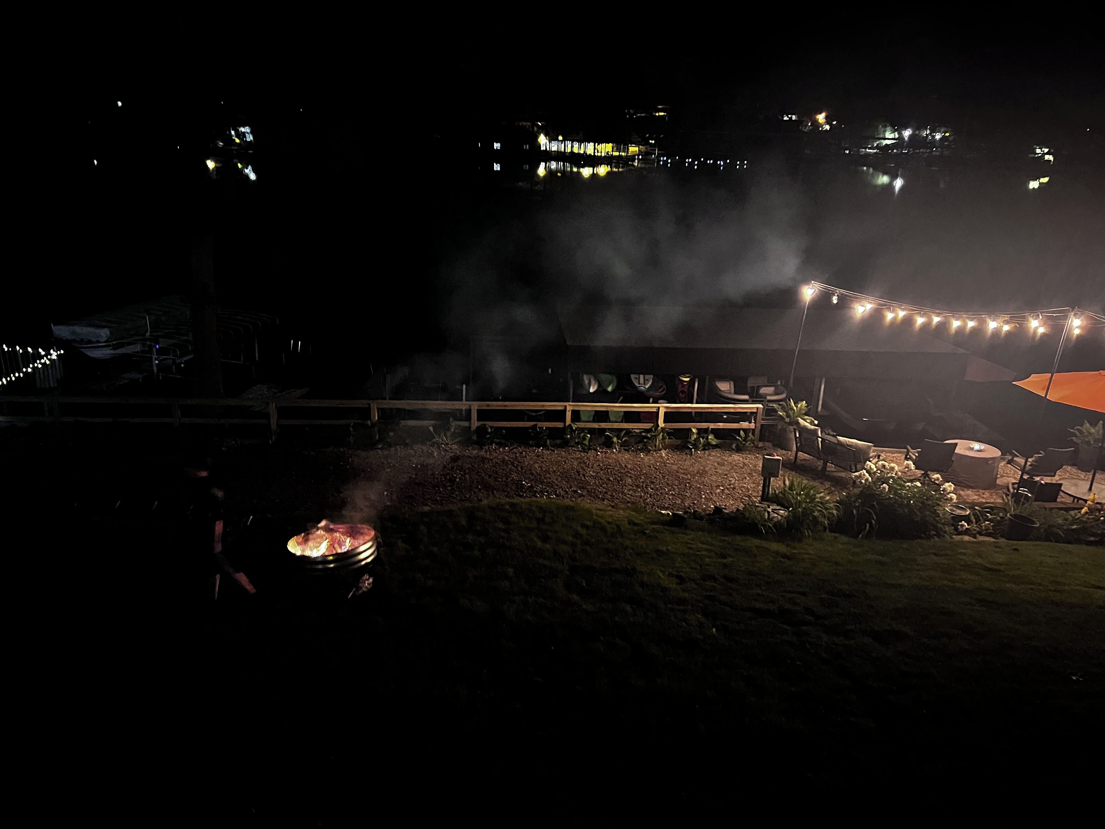 A nighttime outdoor setting with a barbecue grill, a covered seating area, and string lights.