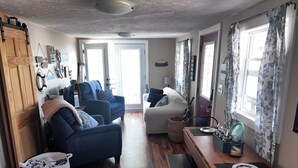 A cozy living room with a sofa, armchair, and a dining table with a bench. There is a basket and a small table with a plate and utensils. - Waterfront 2BR Cottage: Fire Pit, Grill & Dock -Boat Slip Available additional (Monticello)