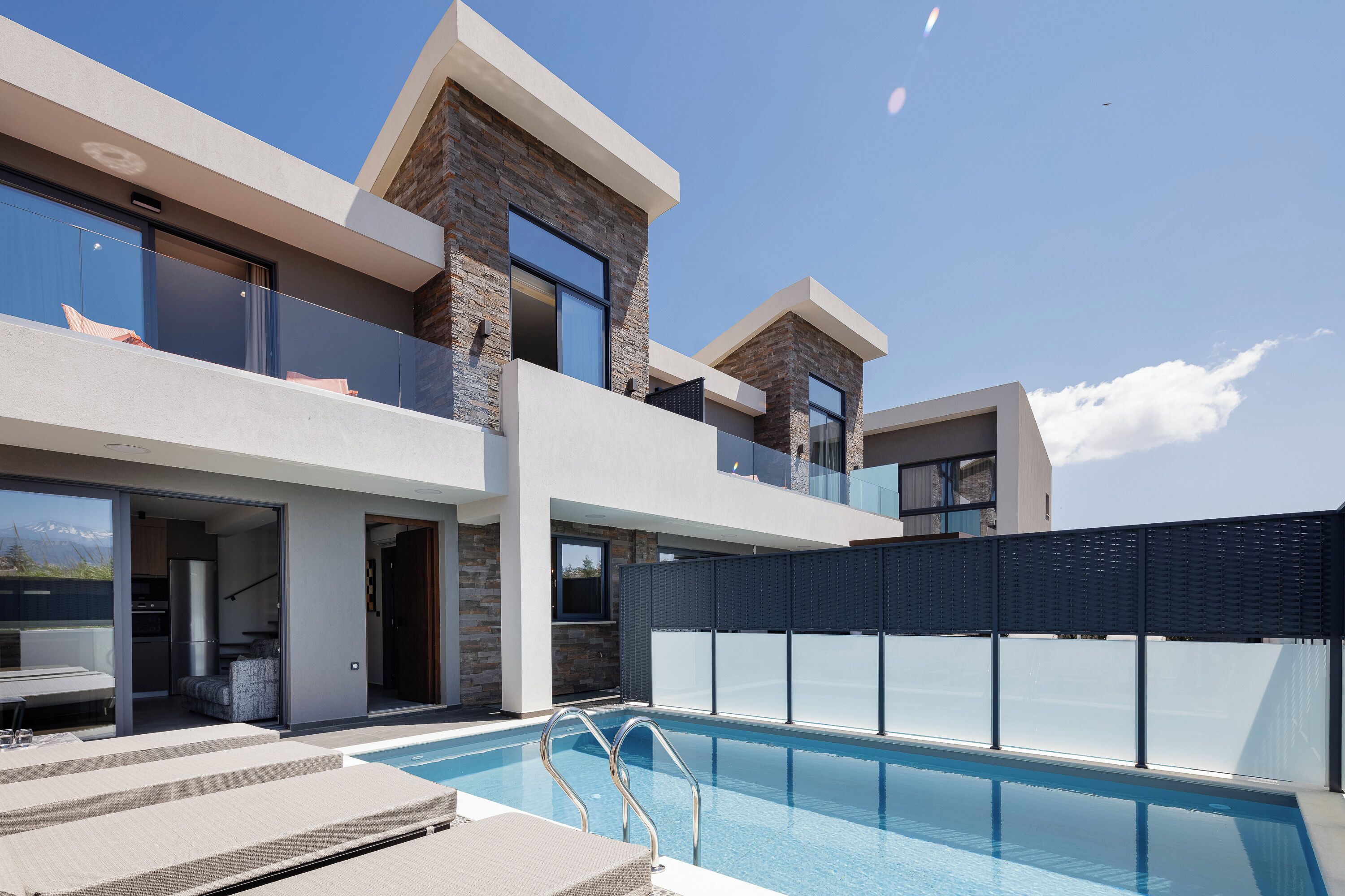 A modern two-story house with a swimming pool, large windows, and a balcony.