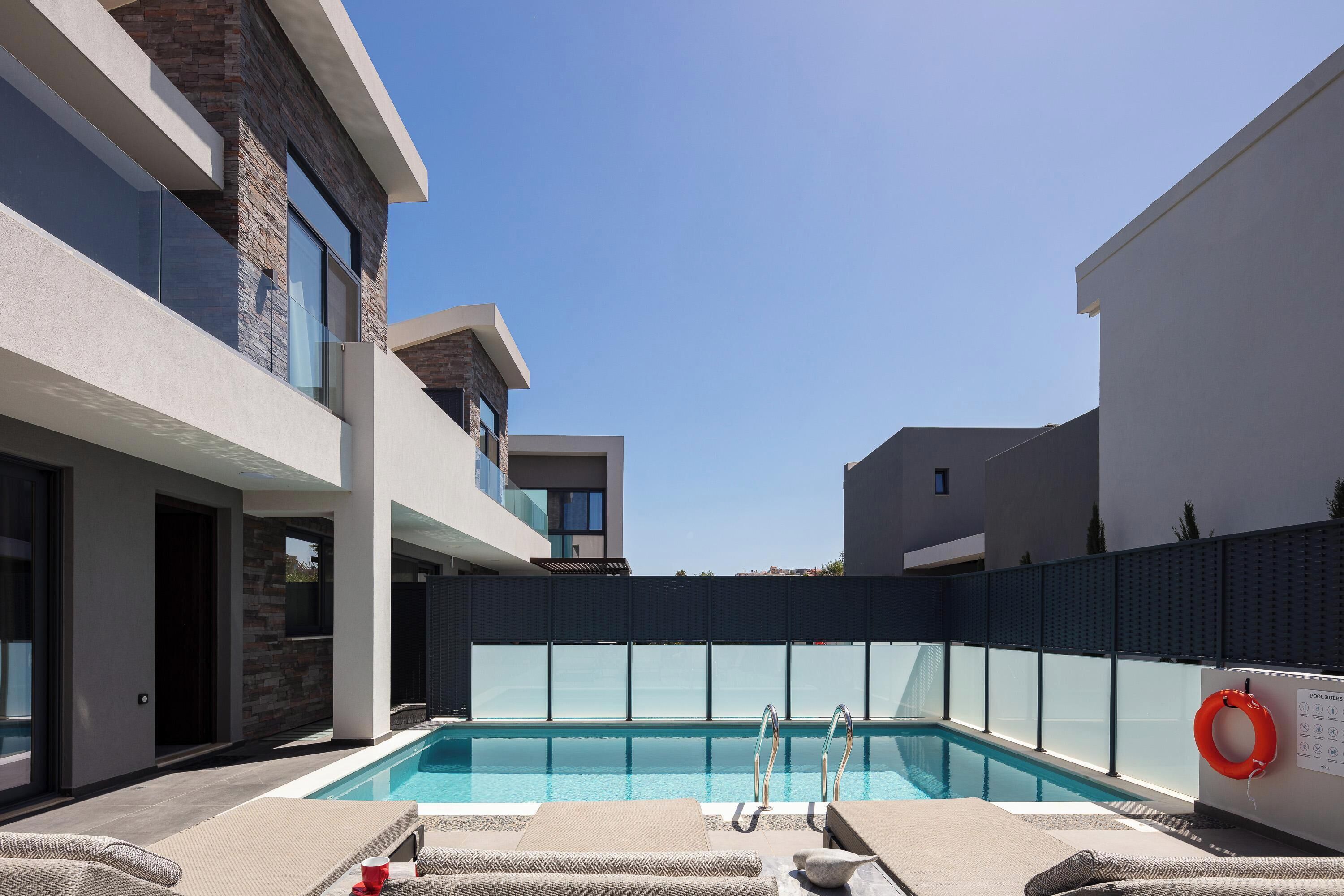 A modern outdoor pool area with lounge chairs, a clear blue pool, and a lifebuoy on the wall.