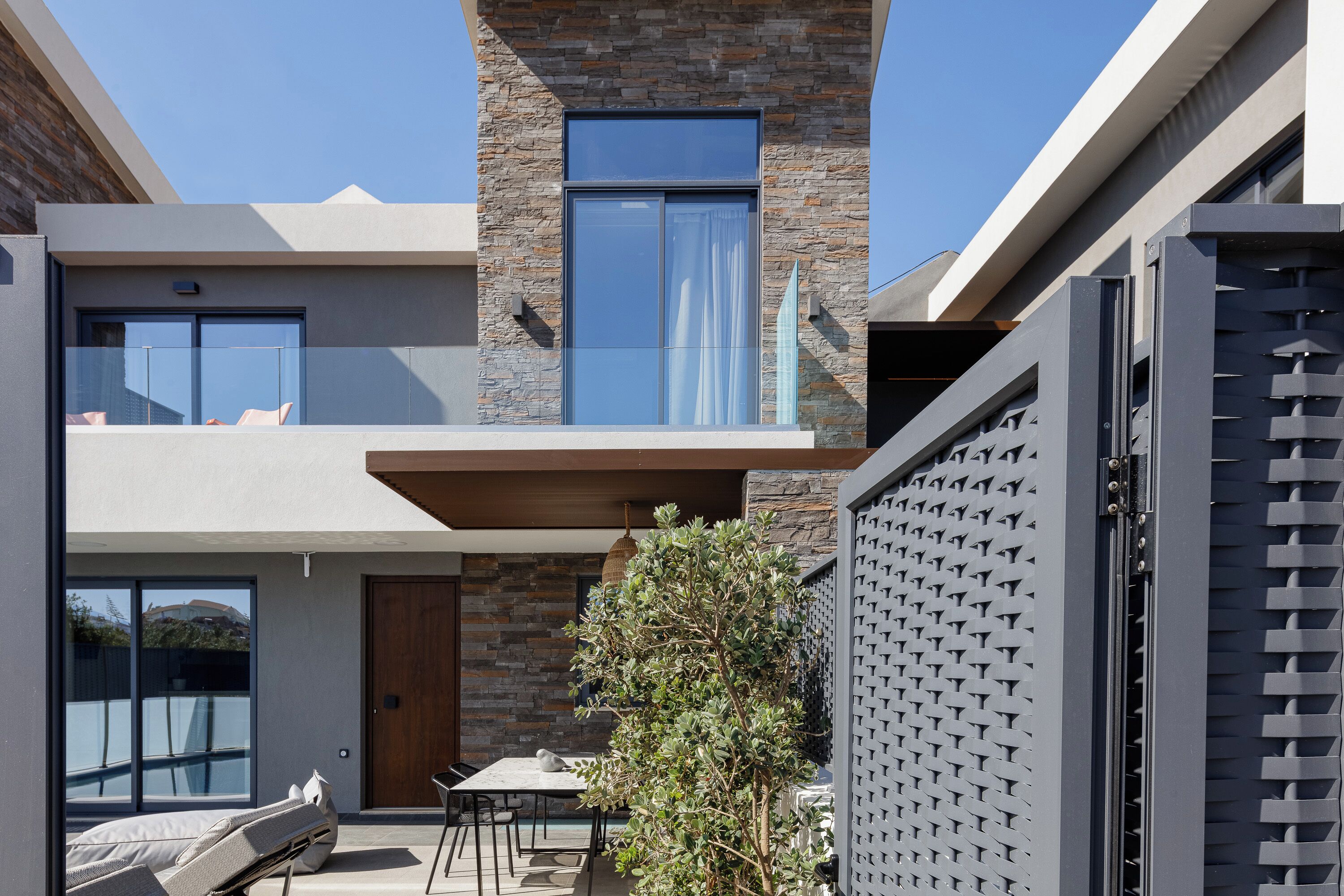 Een modern gebouw met een gevel van natuursteen, een balkon met zitplaatsen en een eethoek met een tafel en stoelen.
