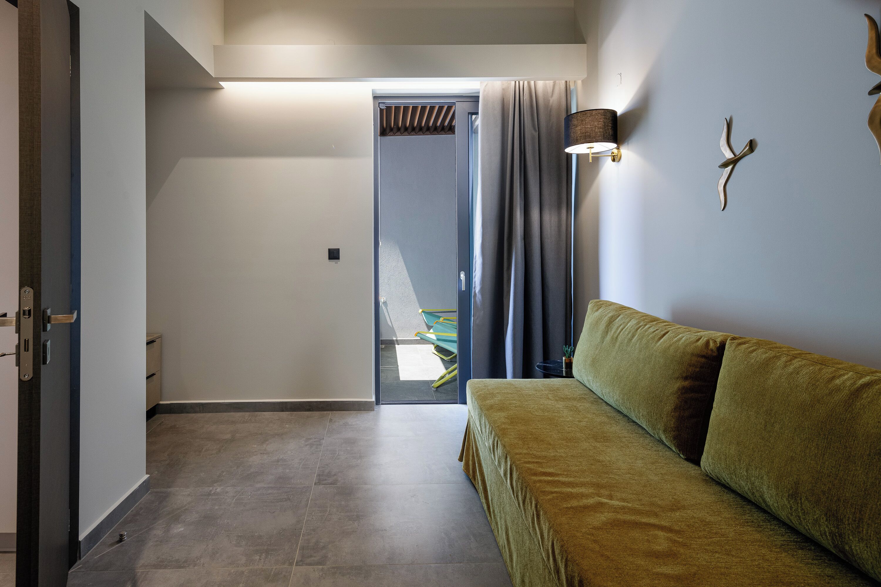 A modern hotel room with a sofa, a lamp, and a door leading to a balcony.