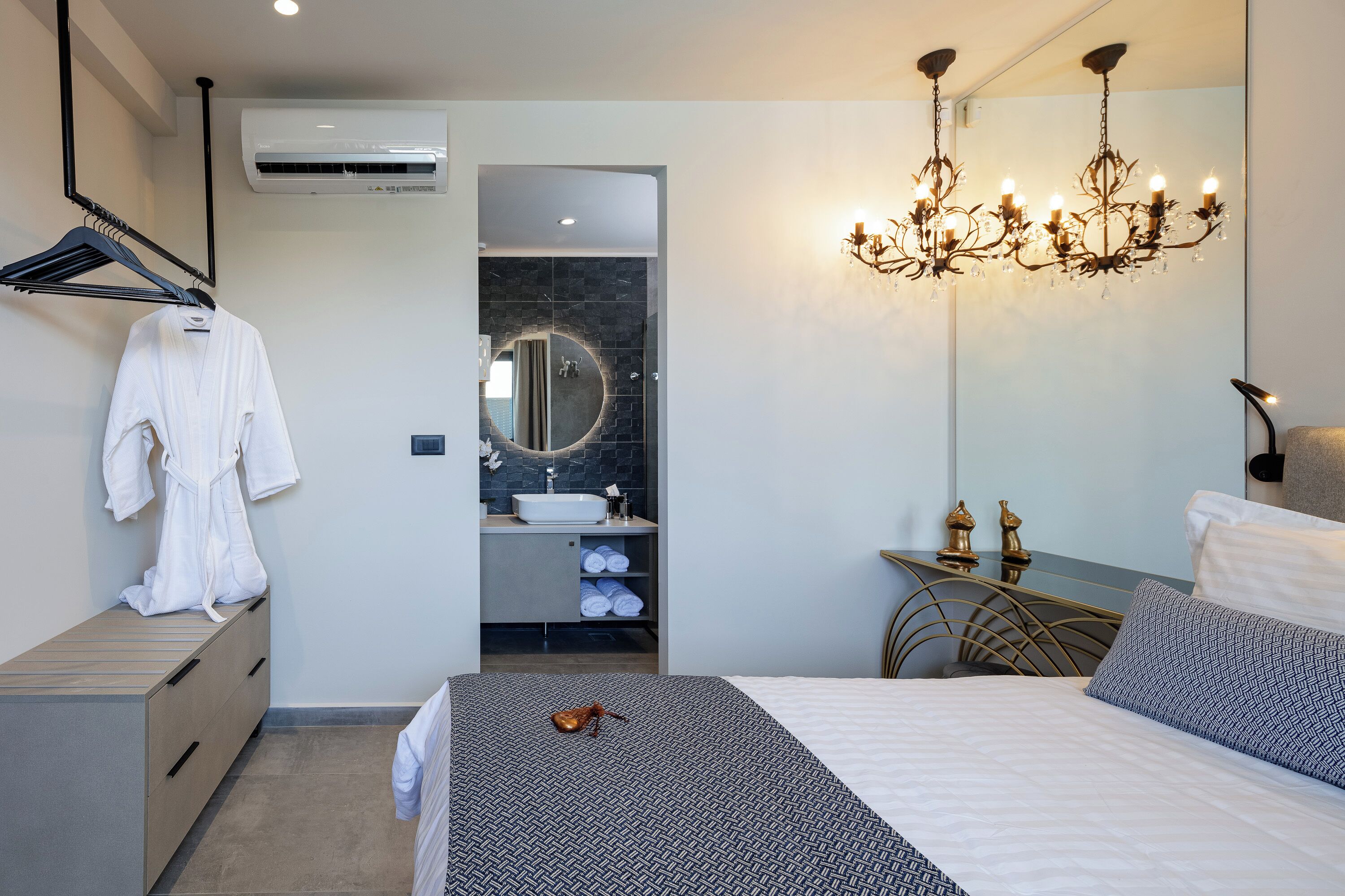 A modern bedroom with a bed, a bedside table, a chandelier, a mirror, and a wardrobe.