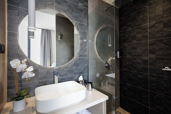 A modern bathroom with a large oval sink, a round mirror, and a glass-enclosed shower.