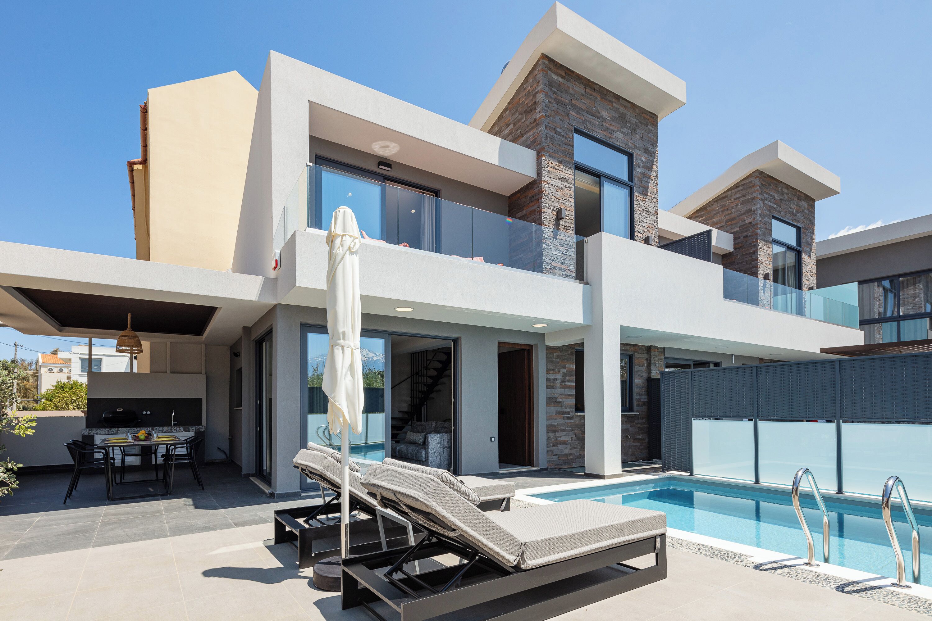 A modern two-story house with a swimming pool, outdoor seating, and a staircase leading to the upper floor.