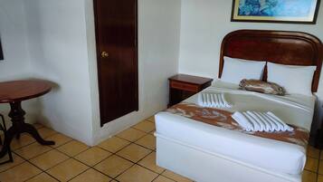 Habitación de hotel con cama, una mesita de madera, una mesita de noche y una puerta.