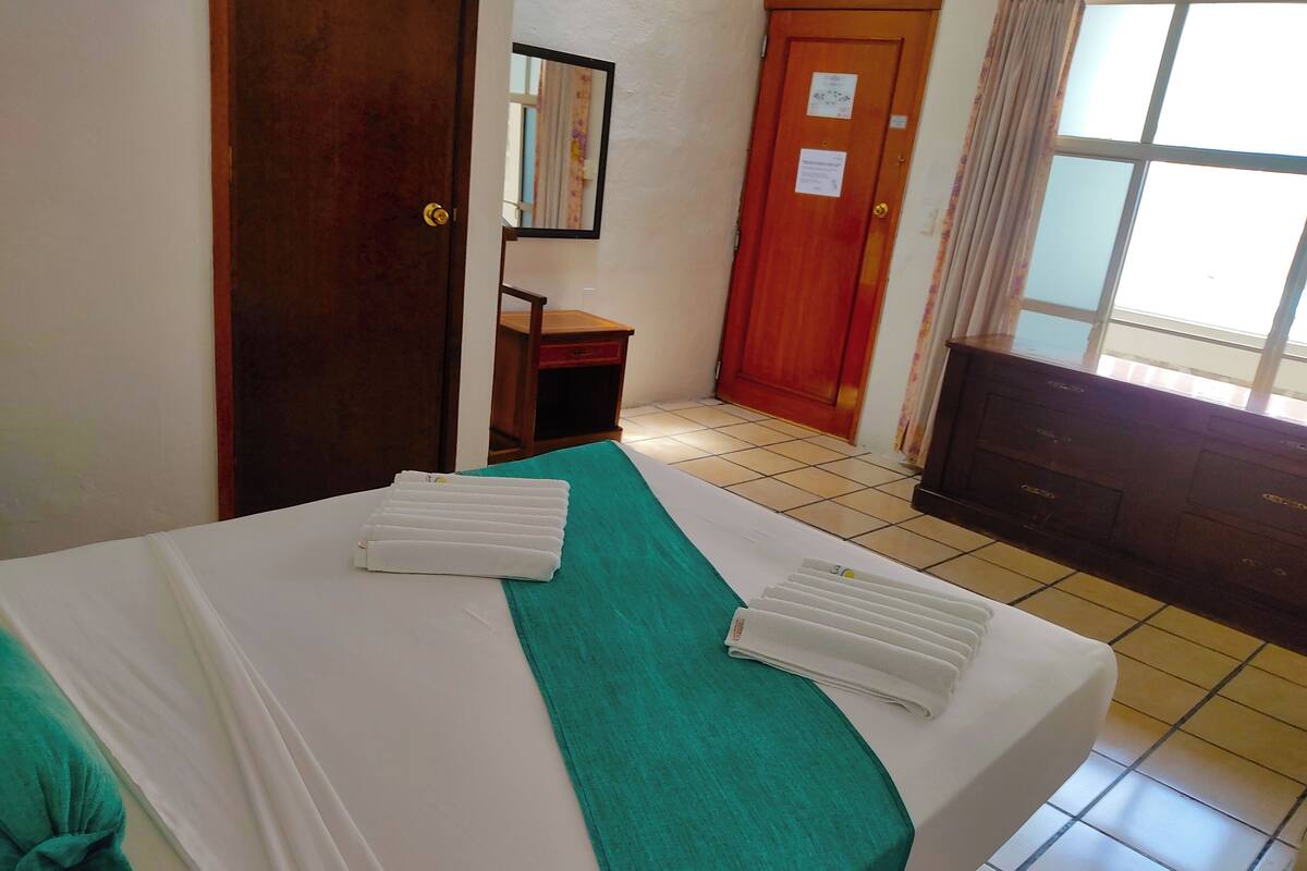 Una camera d'albergo con un letto, una scrivania, un comò, uno specchio e una finestra con tende.