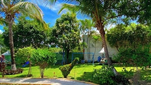 A courtyard with a stone pathway, palm trees, and a fenced play area.