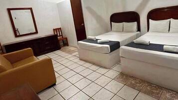 Habitació d'hotel amb dos llits individuals, un sofà, un panell de capçalera de fusta, un mirall i un paviment de rajoles.