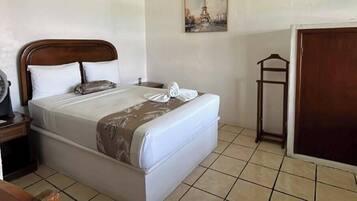 A hotel room with a bed, a bedside table with a fan, a wardrobe, and a wall-mounted picture.