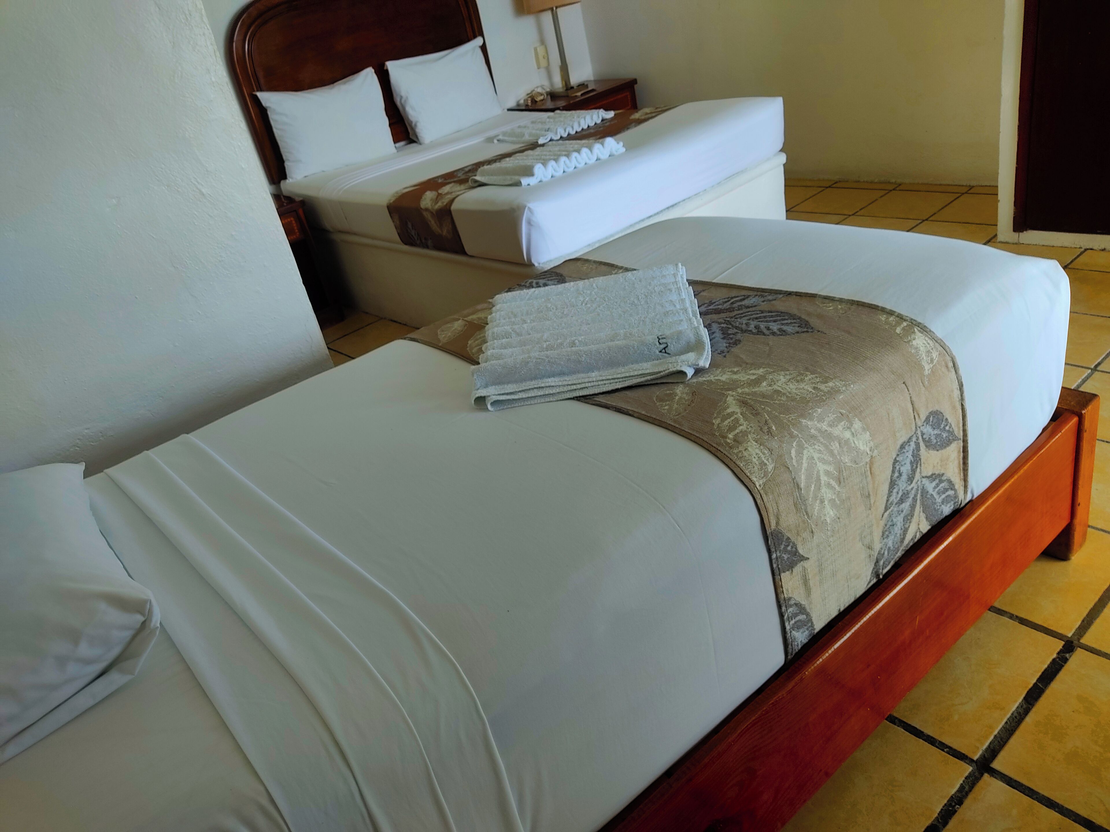Una cama bien hecha con sábanas blancas y un plaid estampado con motivos florales.