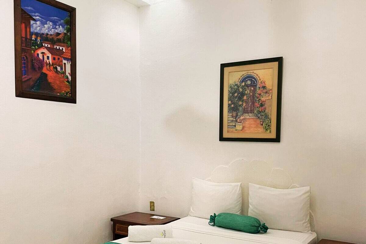 Una camera d'albergo con un letto, un comodino, un quadro incorniciato e una lampada a soffitto.