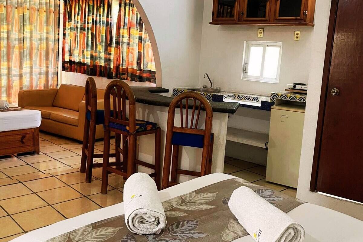 Una camera d'albergo con un letto, due sedie, un angolo cottura e una finestra con tende.