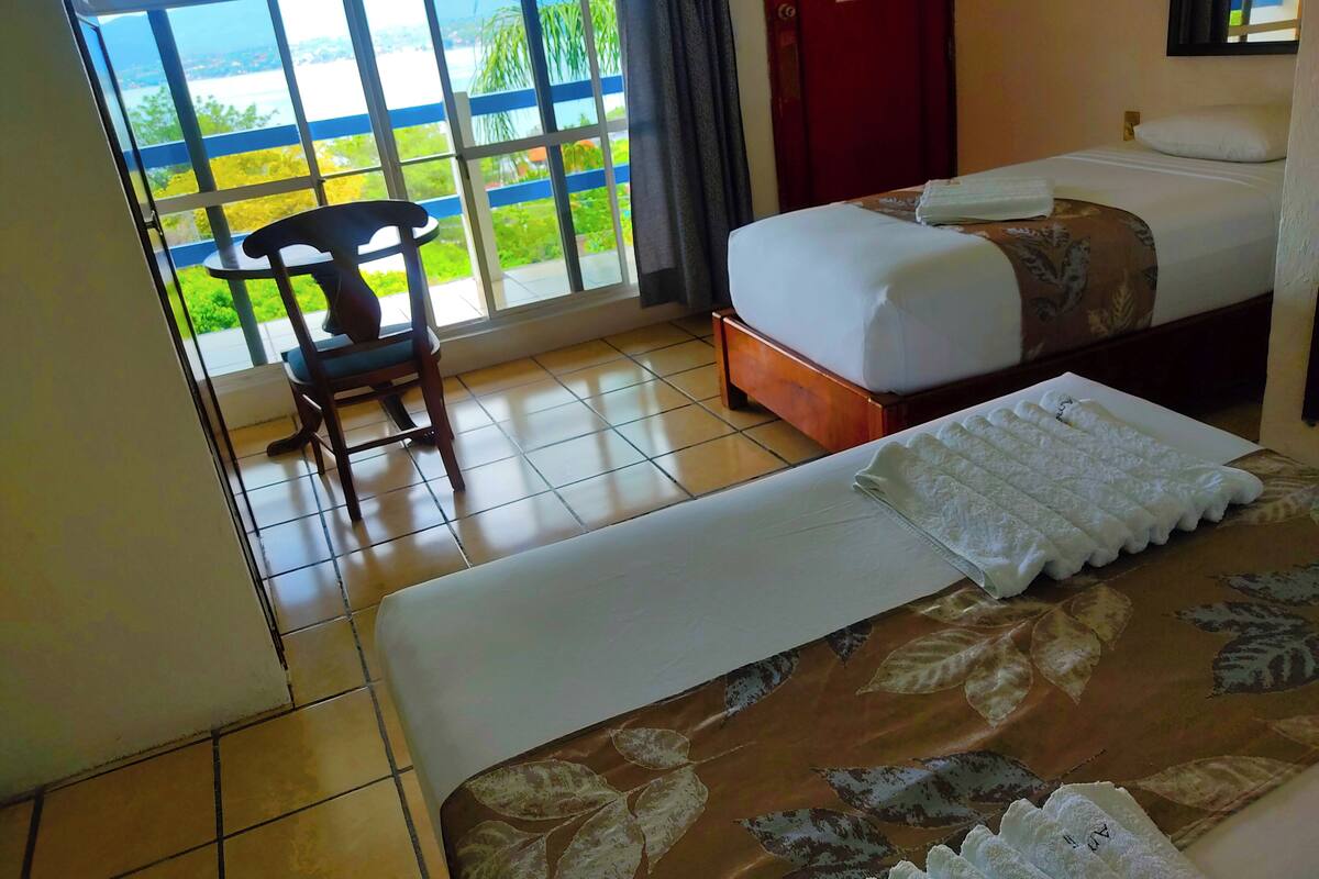 Camera d'albergo con un letto, una sedia e vista su uno specchio d'acqua attraverso ampie finestre.