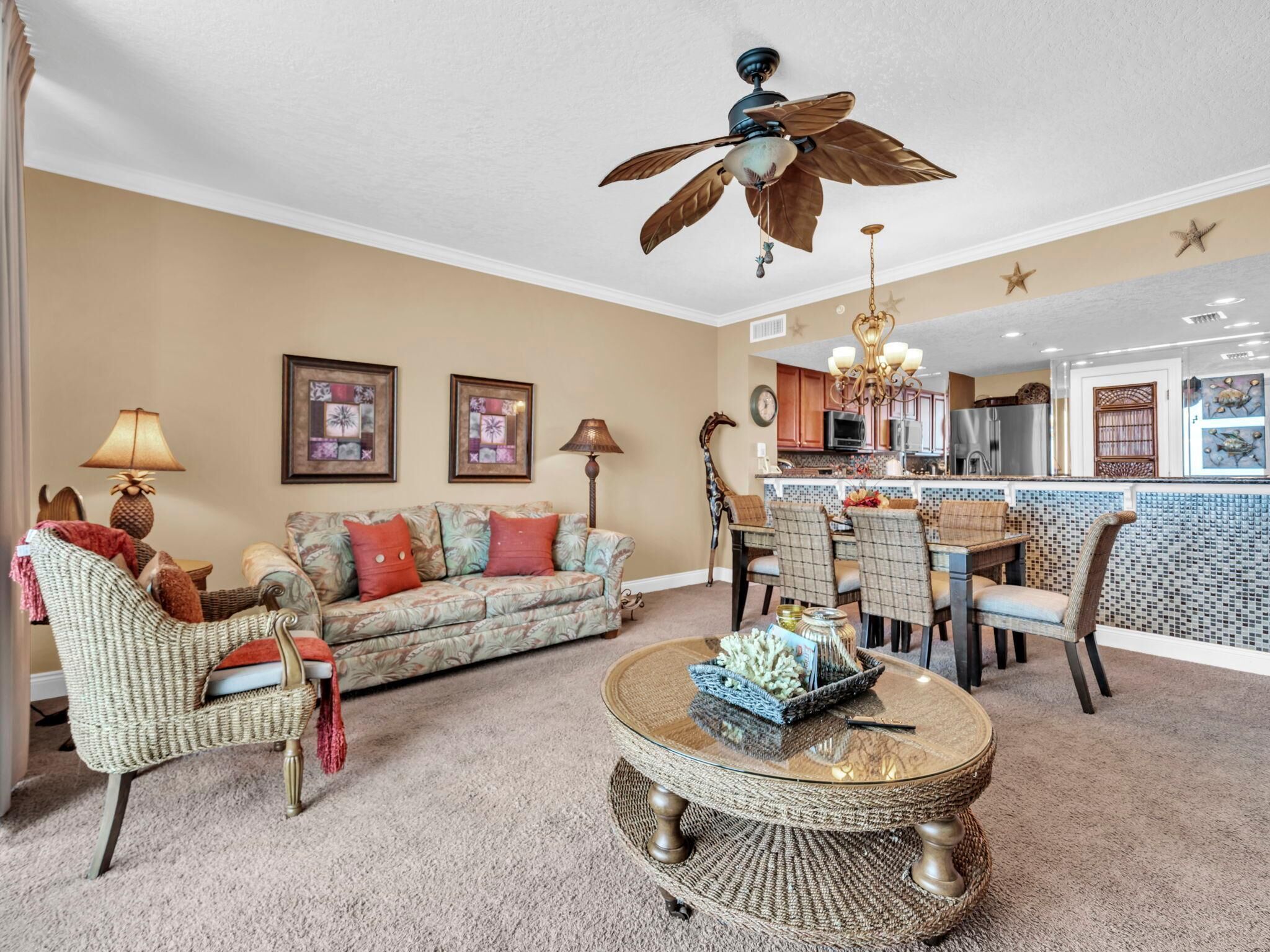 A living room with a sofa, chairs, a coffee table, a ceiling fan, and a kitchen area with a dining table and chairs.