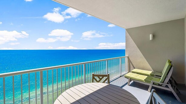 A balcony with a view of the ocean, a table, two chairs, and a small wall-mounted light fixture.