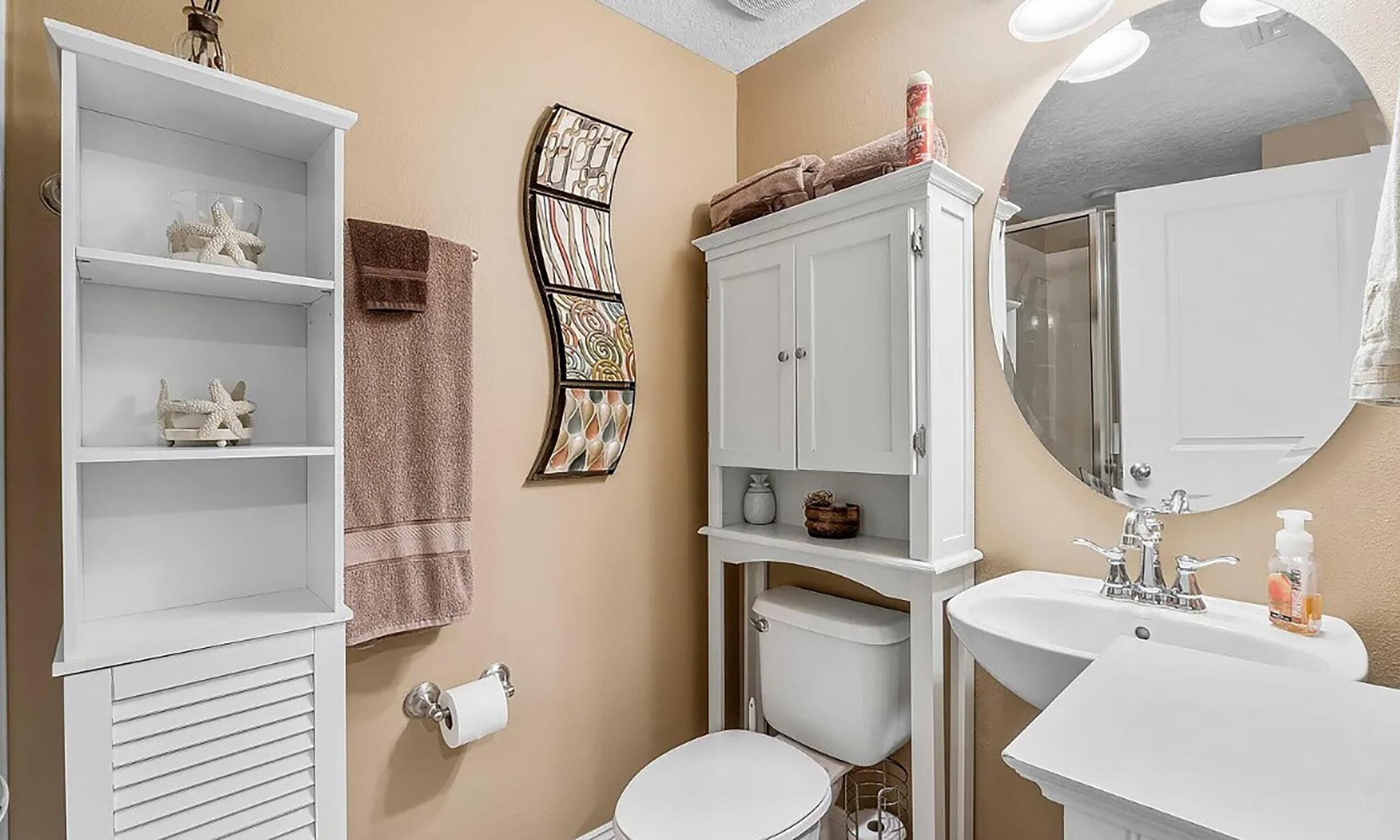 A bathroom with a toilet, sink, and shelves with decorative items.