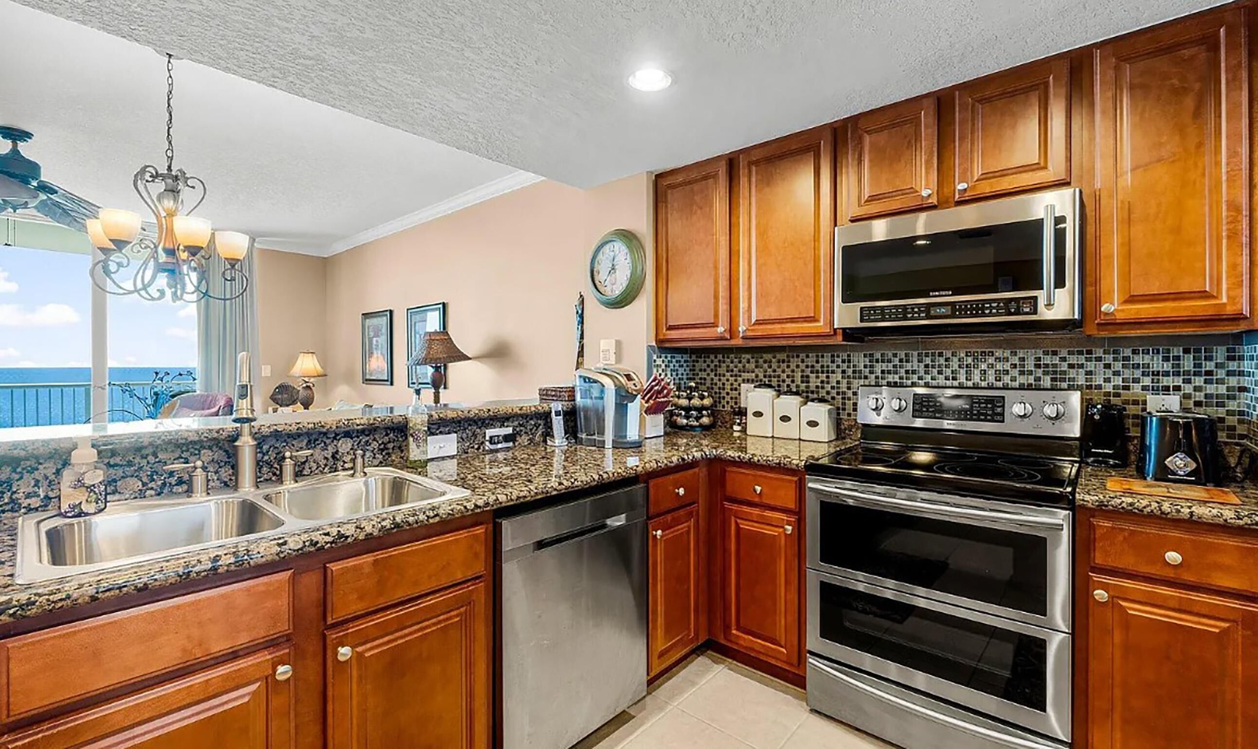 A kitchen with wooden cabinets, stainless steel appliances, a granite countertop, and a view of the ocean.