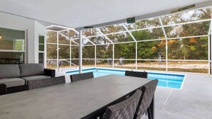 Ett takförsett utomhusområde med en pool, sittplatser och utsikt över träd.