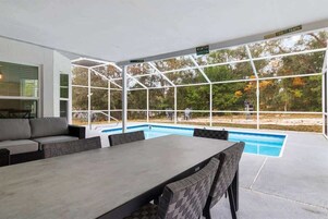 Un espacio al aire libre cubierto con piscina, asientos y vistas a árboles.