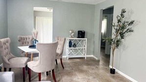 A dining area with a white table and four chairs, a white console table with a coffee maker, and a potted plant. - Cozy 2 Bedroom Home, Dade City! #2 (Dade City)