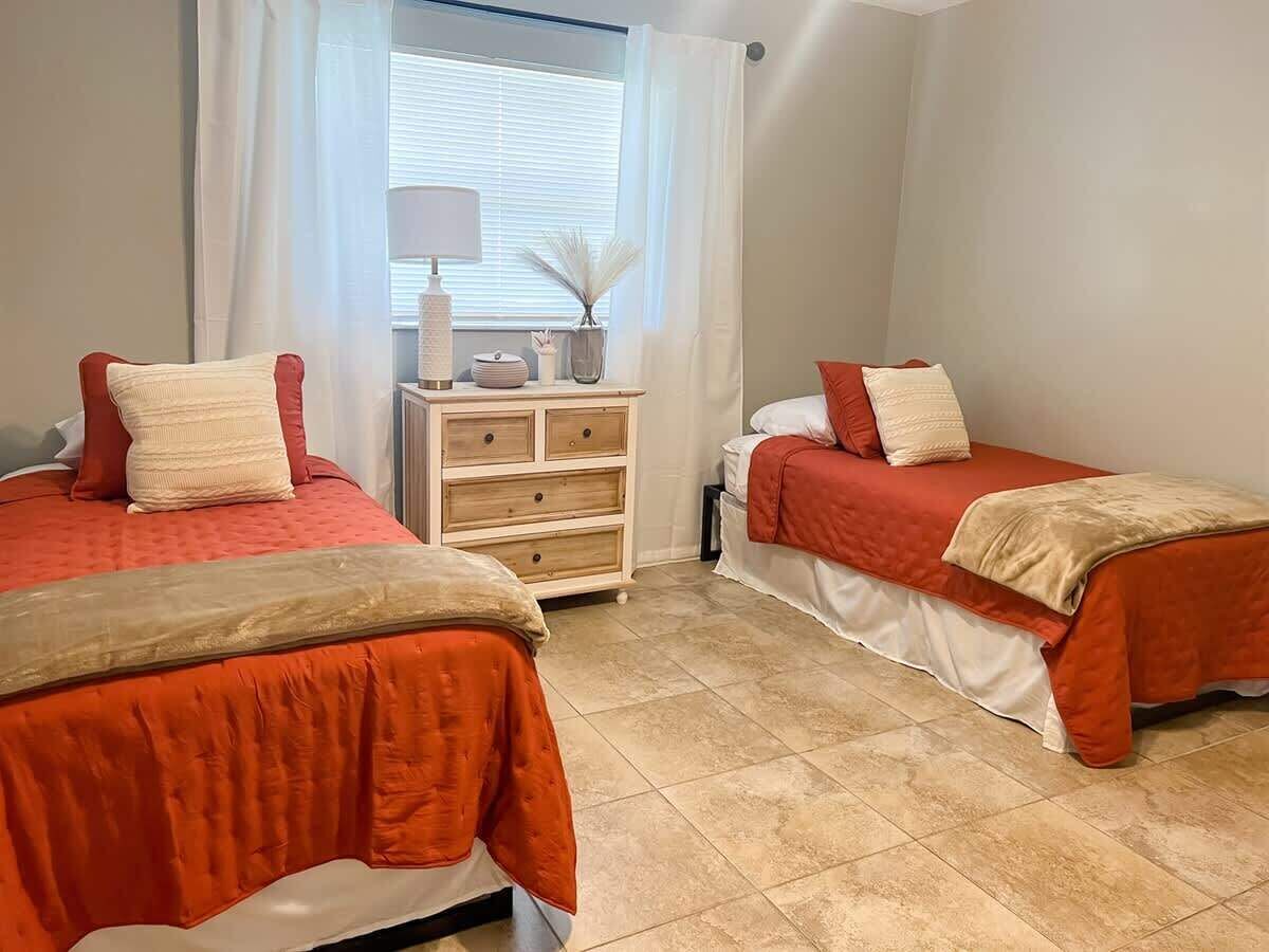 A bedroom with two beds, a nightstand, and a window with curtains.