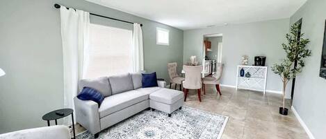 A modern living room with a sectional sofa, a small round table, and a dining area with chairs.