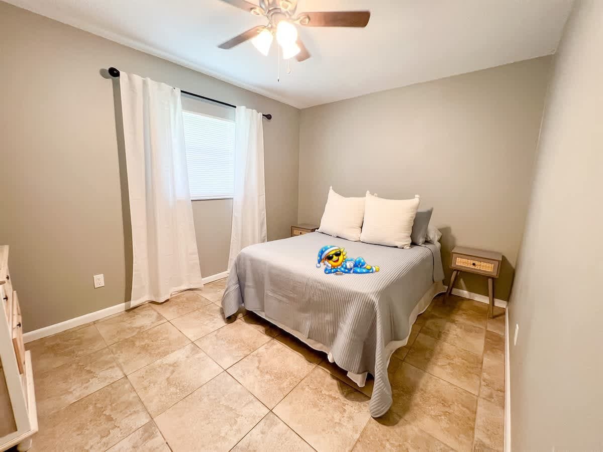 A bedroom with a bed, a ceiling fan, a window with curtains, and a bedside table.
