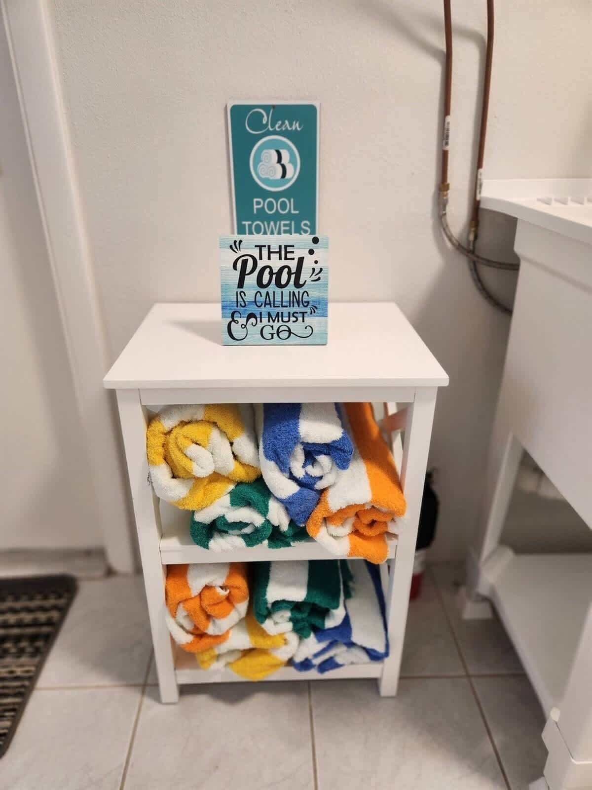 A white shelf with colorful towels and a sign that reads "Clean Pool Towels".