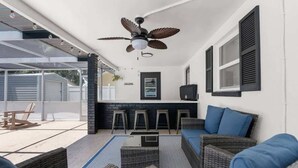 Un espace extérieur aménagé en terrasse, avec des meubles en osier, un ventilateur de plafond et un coin bar équipé de tabourets.