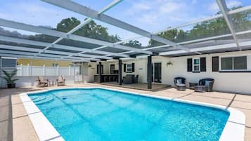 Una piscina con un patio techado, mobiliario exterior y un bar.