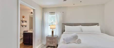 A hotel room with a bed, a nightstand, a ceiling fan, and a bathroom visible through an open door.