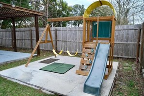 A wooden swing set with a slide, green rubber mats, and a covered seating area. - Brooksville Retreat! 3 Bed, 2 Bath! (Brooksville)