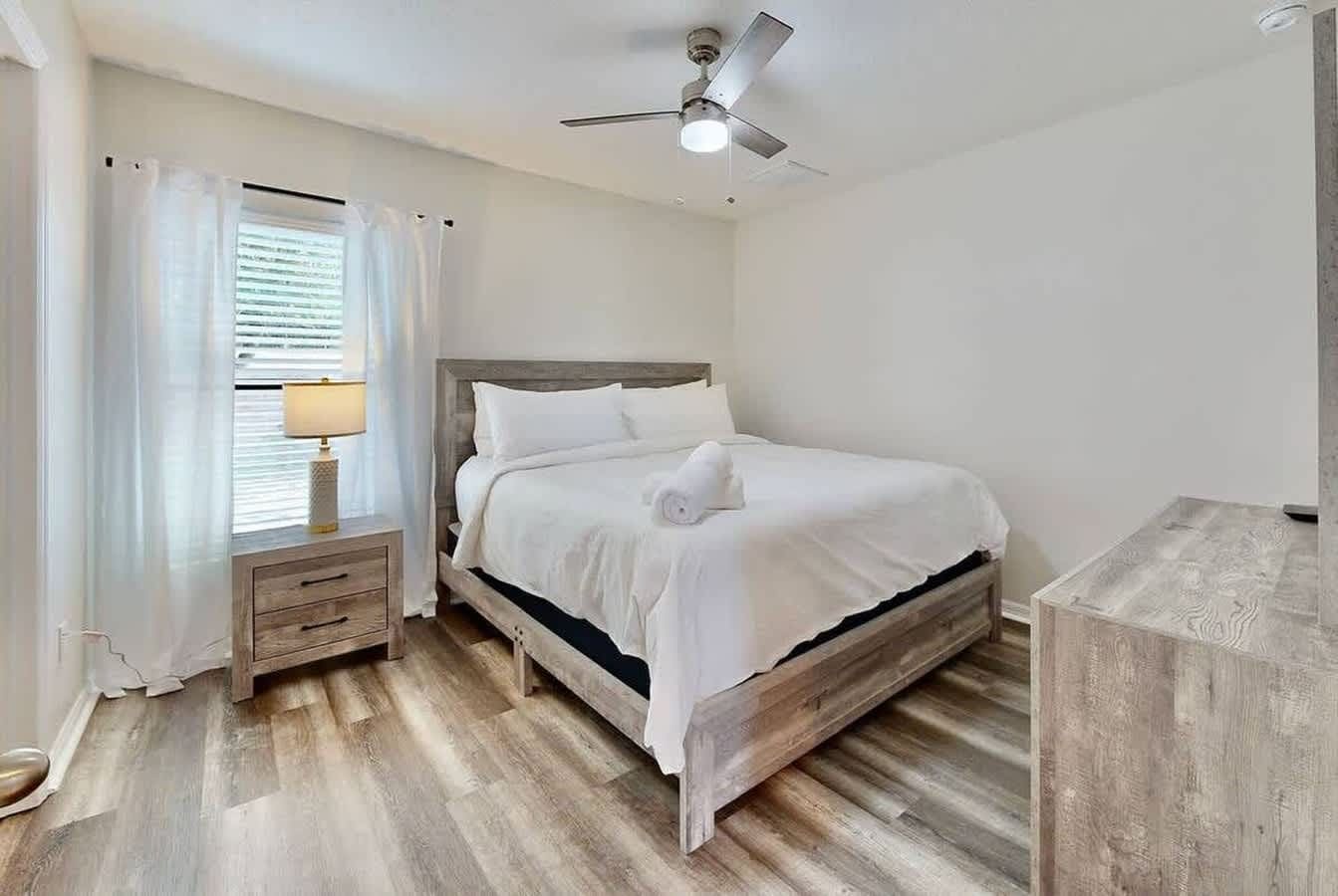 Une chambre à coucher avec un lit, une table de chevet, une lampe et un ventilateur de plafond.
