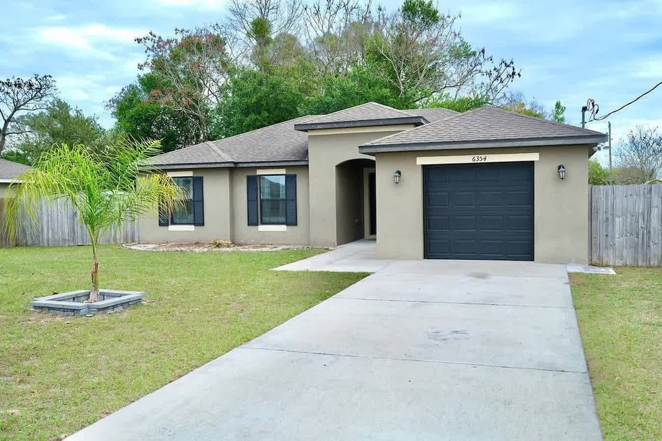 A residential house with a garage, a driveway, and a small tree in the front yard.