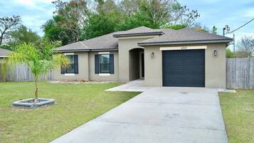 A residential house with a garage, a driveway, and a small tree in the front yard.