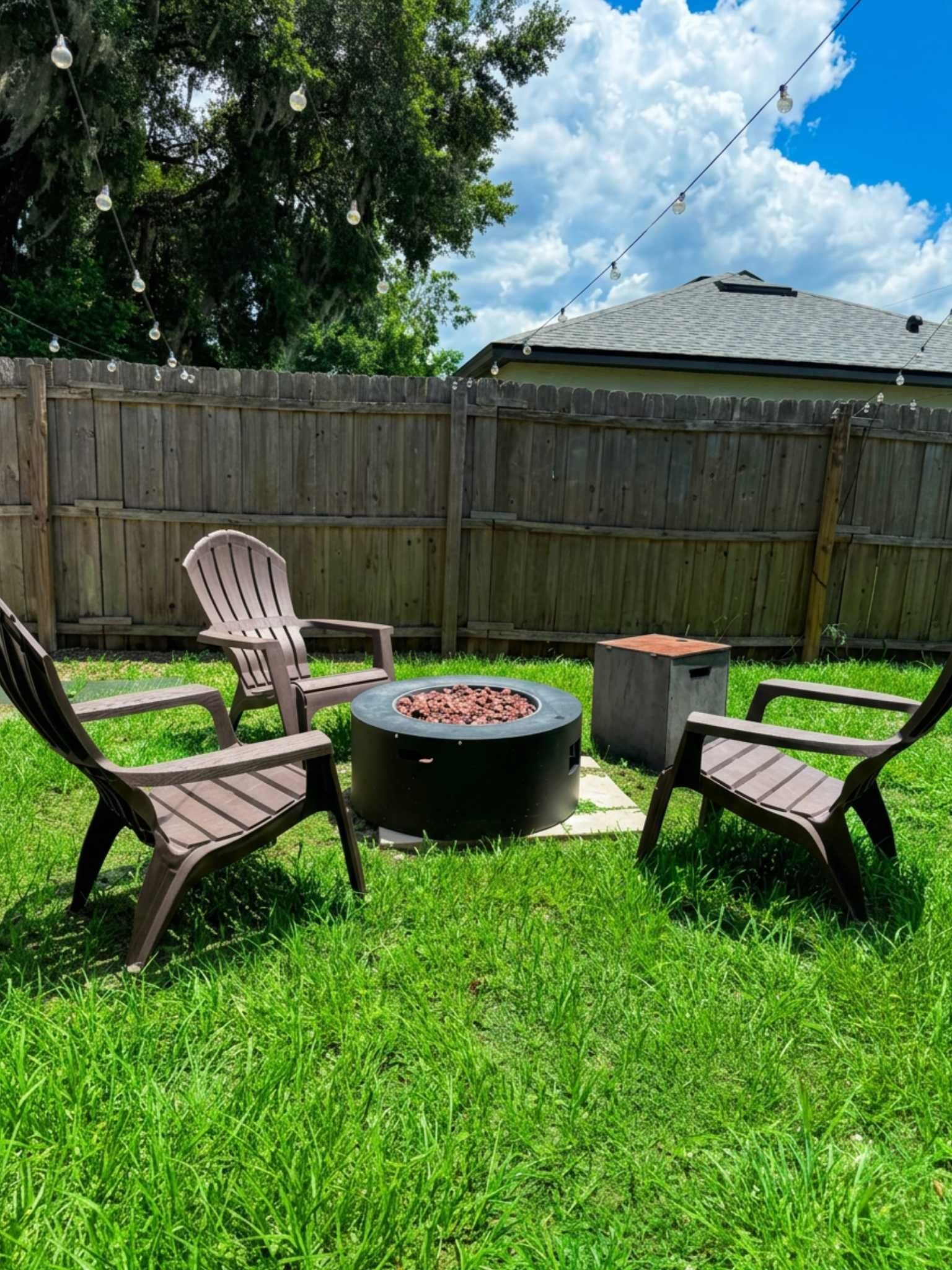 A backyard with a circular fire pit, two Adirondack chairs, and a wooden fence.