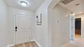 Corredor com uma porta branca, uma luminária no teto e um respiradouro de ar na parede.