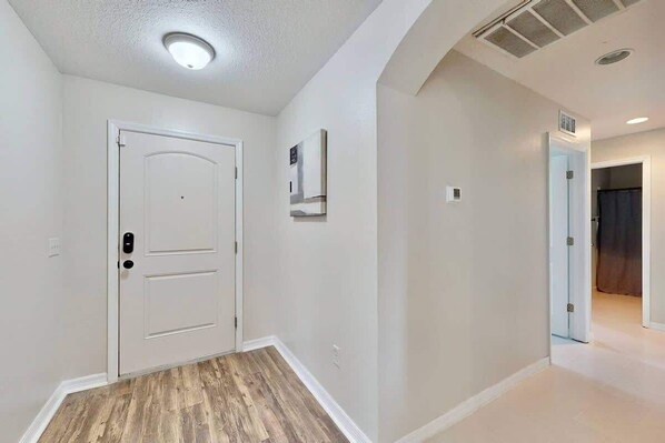 A hallway with a white door, a ceiling light, and a wall-mounted air vent. - Brooksville Retreat! 3 Bed, 2 Bath! (Brooksville)