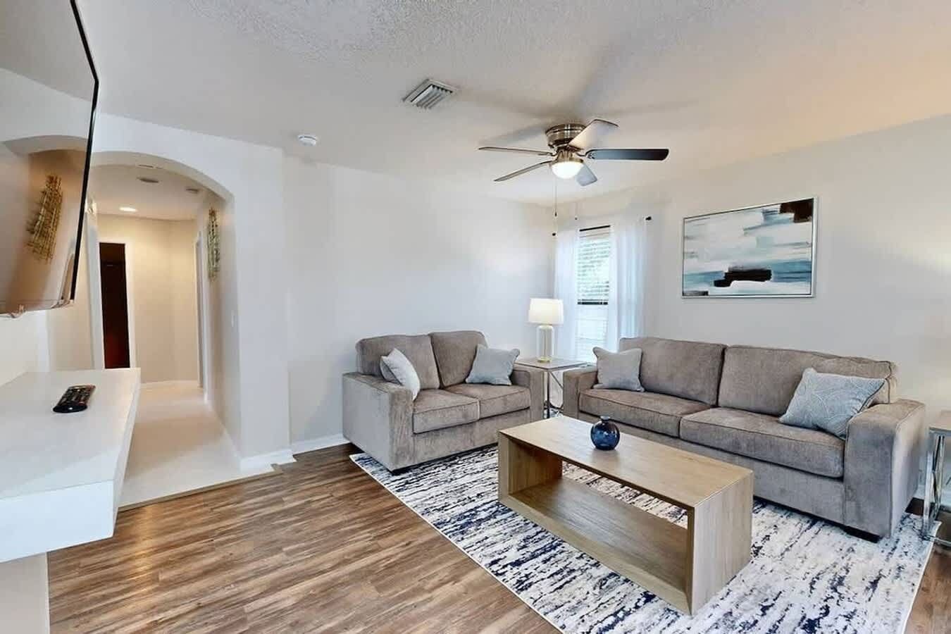 A modern living room with a sofa, two armchairs, a coffee table, and a ceiling fan.