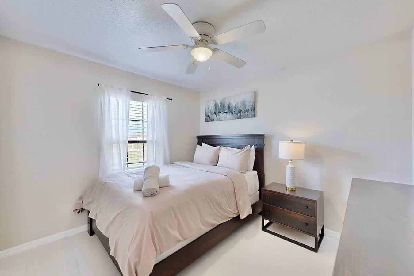 A bedroom with a bed, a nightstand, a ceiling fan, and a window with curtains.