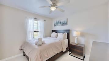 A bedroom with a bed, a nightstand, a ceiling fan, and a window with curtains.