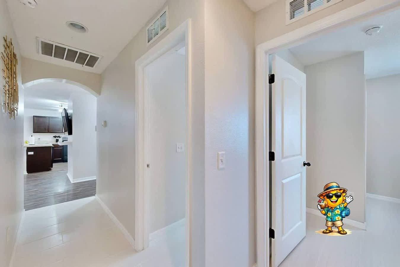 A hallway with white walls and doors leading to a kitchen area.