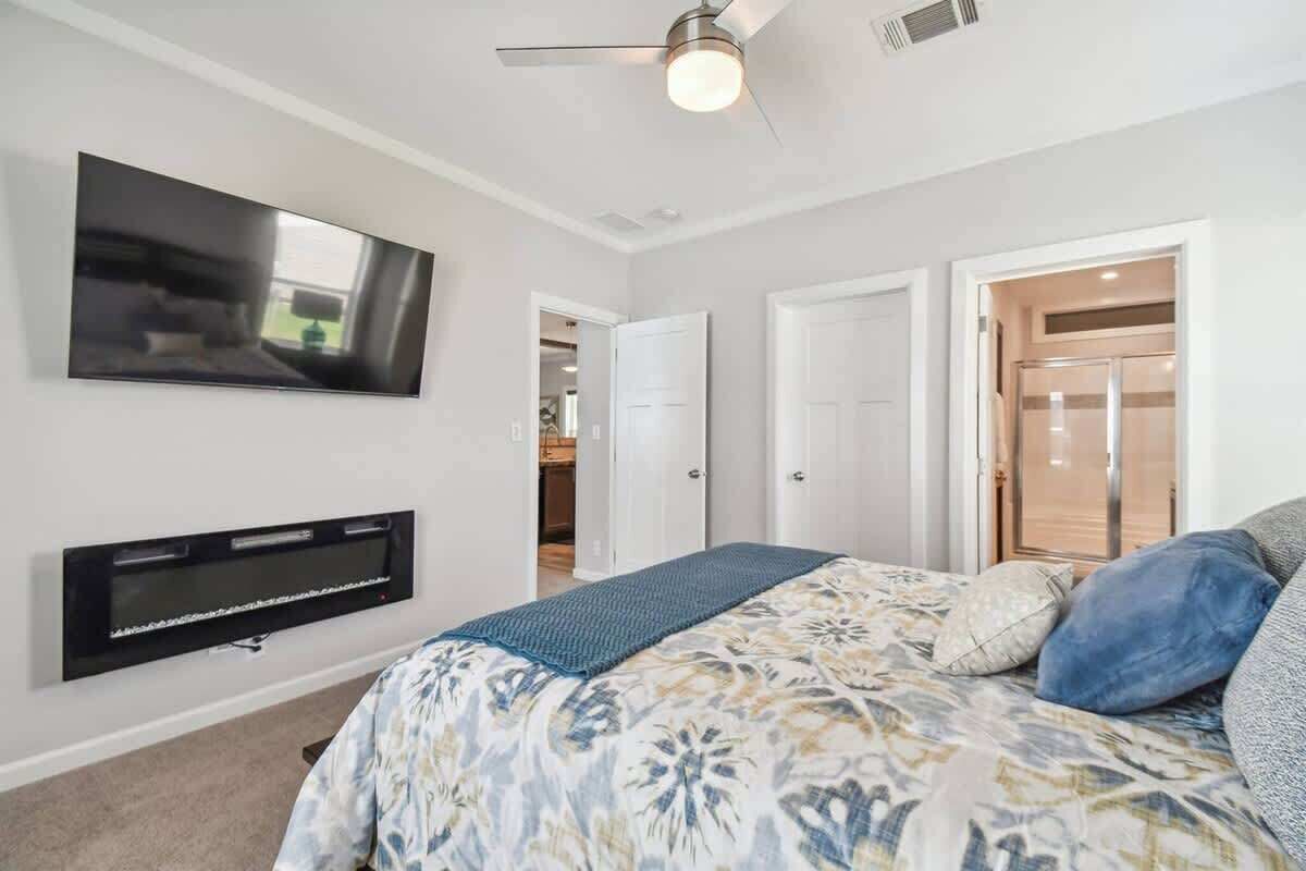 A bedroom with a bed, a flat-screen TV mounted on the wall, and a ceiling fan.