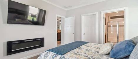 A bedroom with a bed, a flat-screen TV mounted on the wall, and a ceiling fan.
