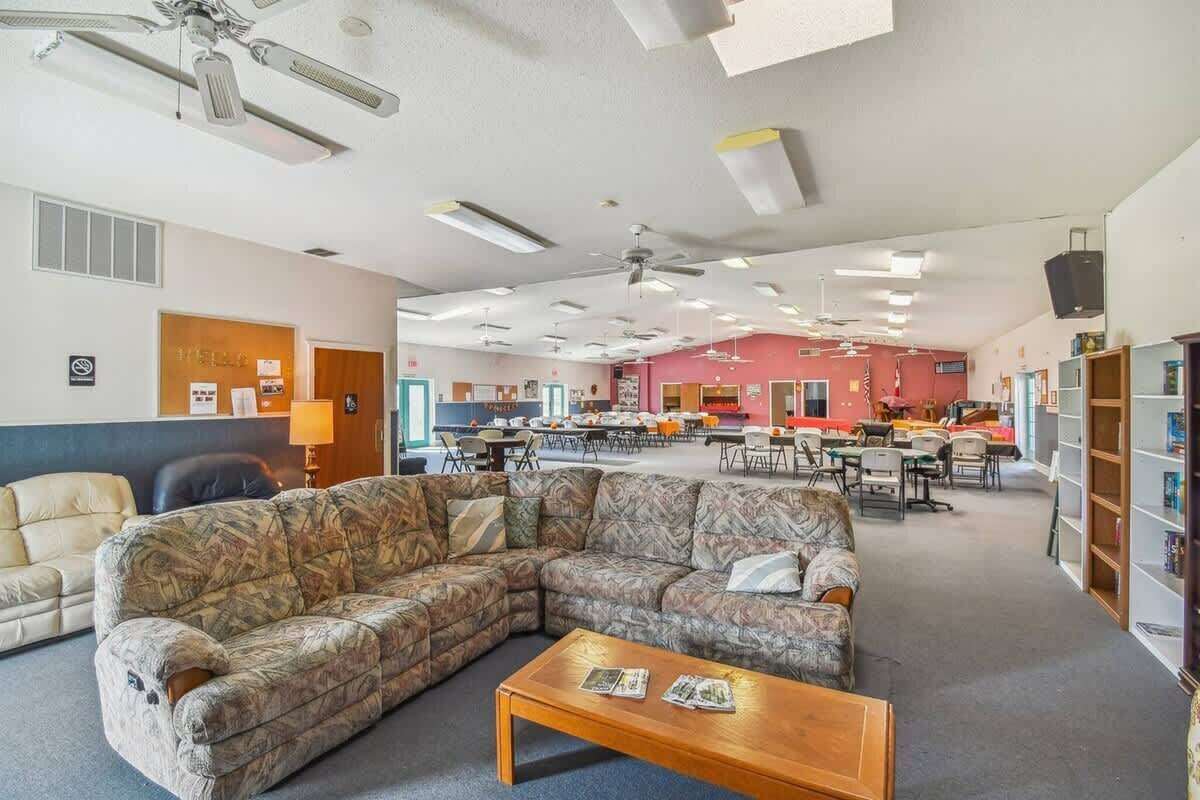 A spacious library with a large sectional sofa, multiple tables, and ceiling fans.